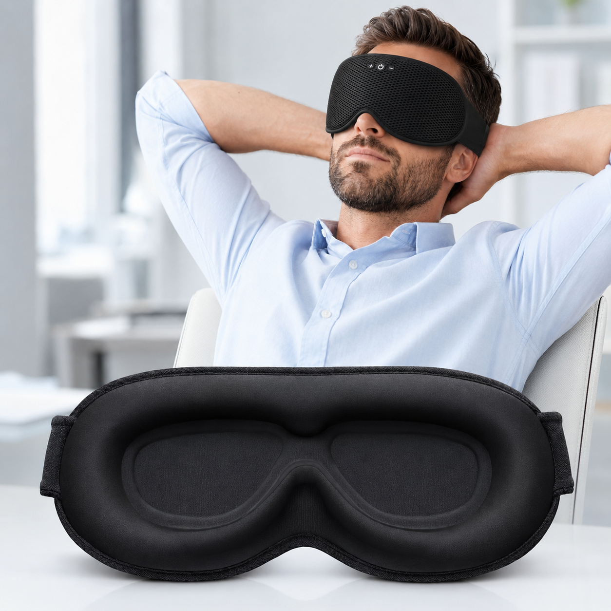 A black Bluetooth sleep mask headphones shown in two views: one worn by a man in a light blue shirt with his arms behind his head, and one laid flat on a white surface in the foreground.