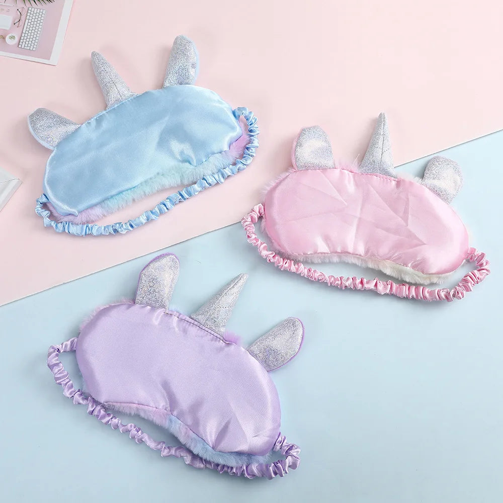Three unicorn-themed sleep masks in blue, pink, and purple on a pastel background.