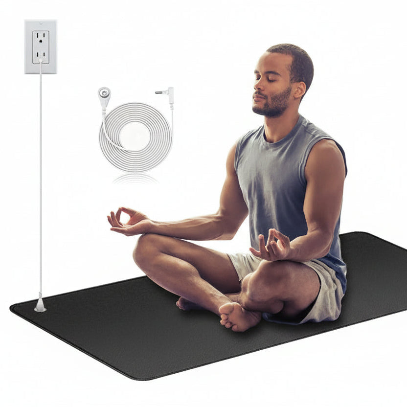 Man meditating on a black mat with a power outlet, cable, and lamp in the background.