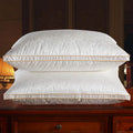 Two white pillows with gold stitching on a wooden surface.