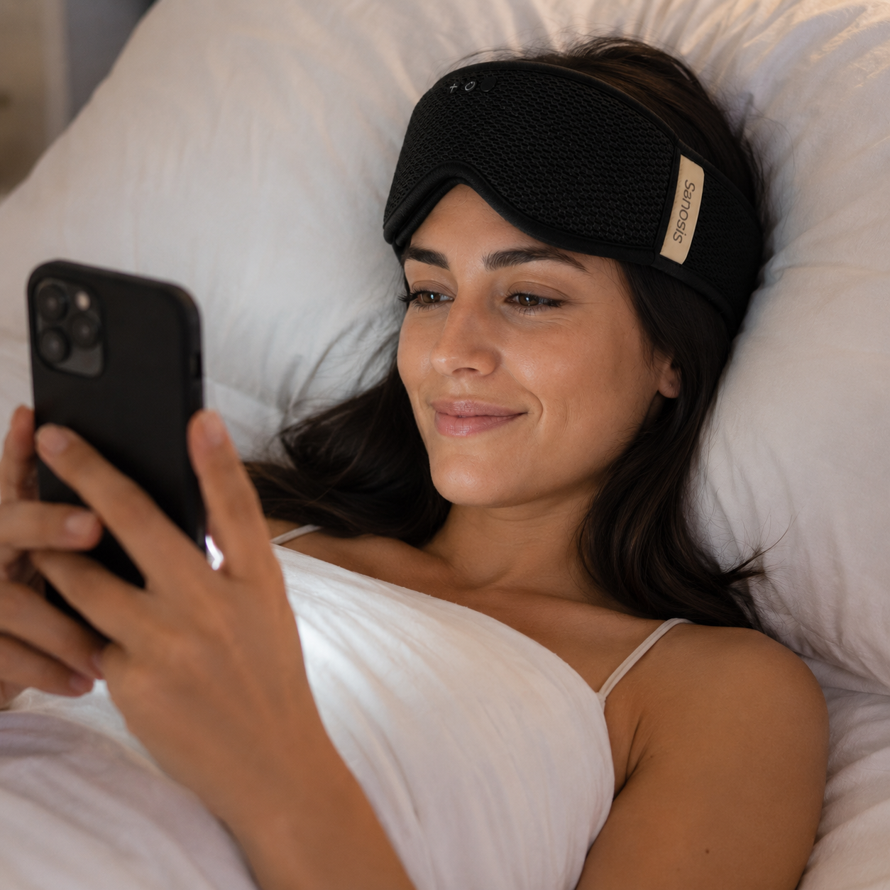 Woman lying in bed using a smartphone with a sleep mask on