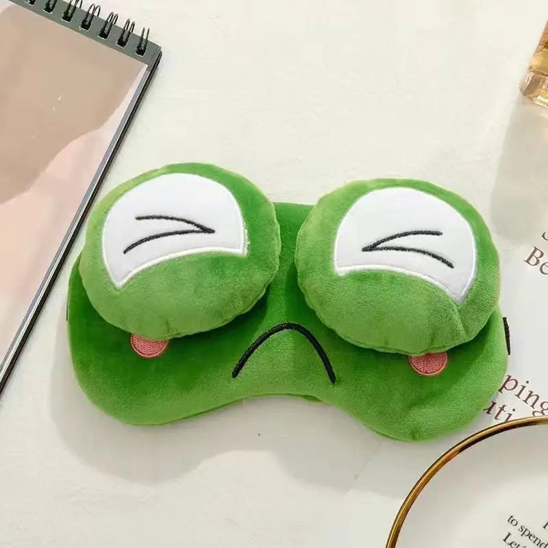 Green plush eye mask with frog design on a white surface
