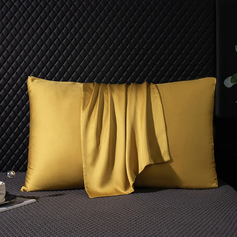 Two mustard yellow satin pillows on a textured surface with a dark background
