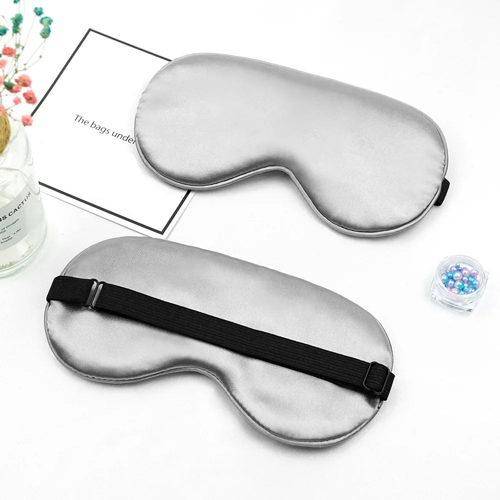 Two silver sleep masks on a white surface with and decorative items.